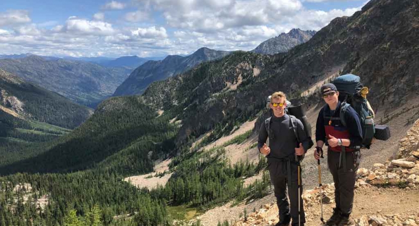 two students pause for a photo in front of a mountain landscape while hiking in the pacific northwest